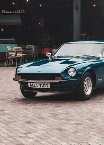 A teal Datsun 260Z parked outside a restaurant at dusk