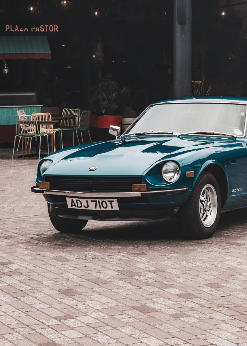 A teal Datsun 260Z parked outside a restaurant at dusk